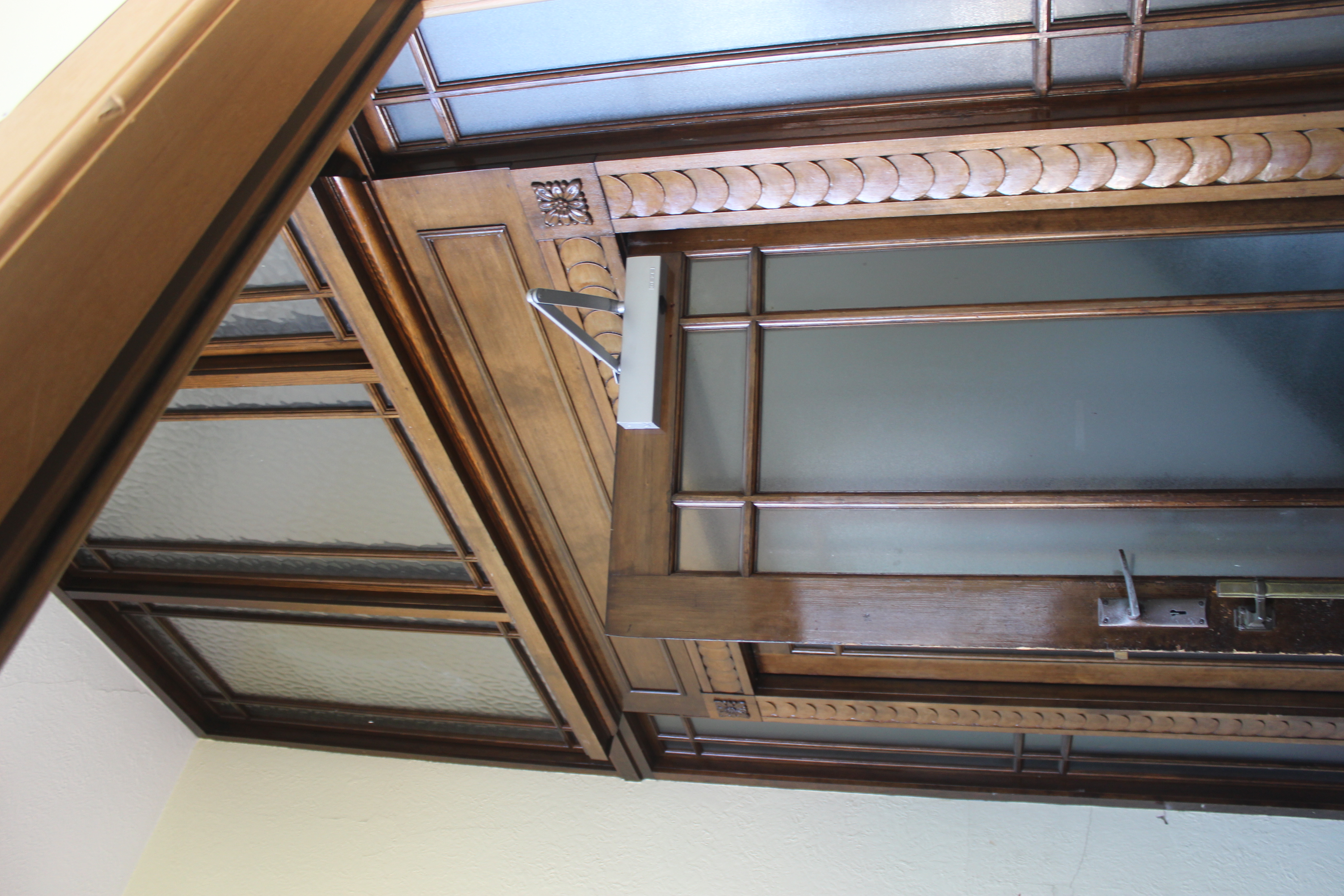 View of internal glazed doorway with decorative carving in wooden frame. The door is partly open.