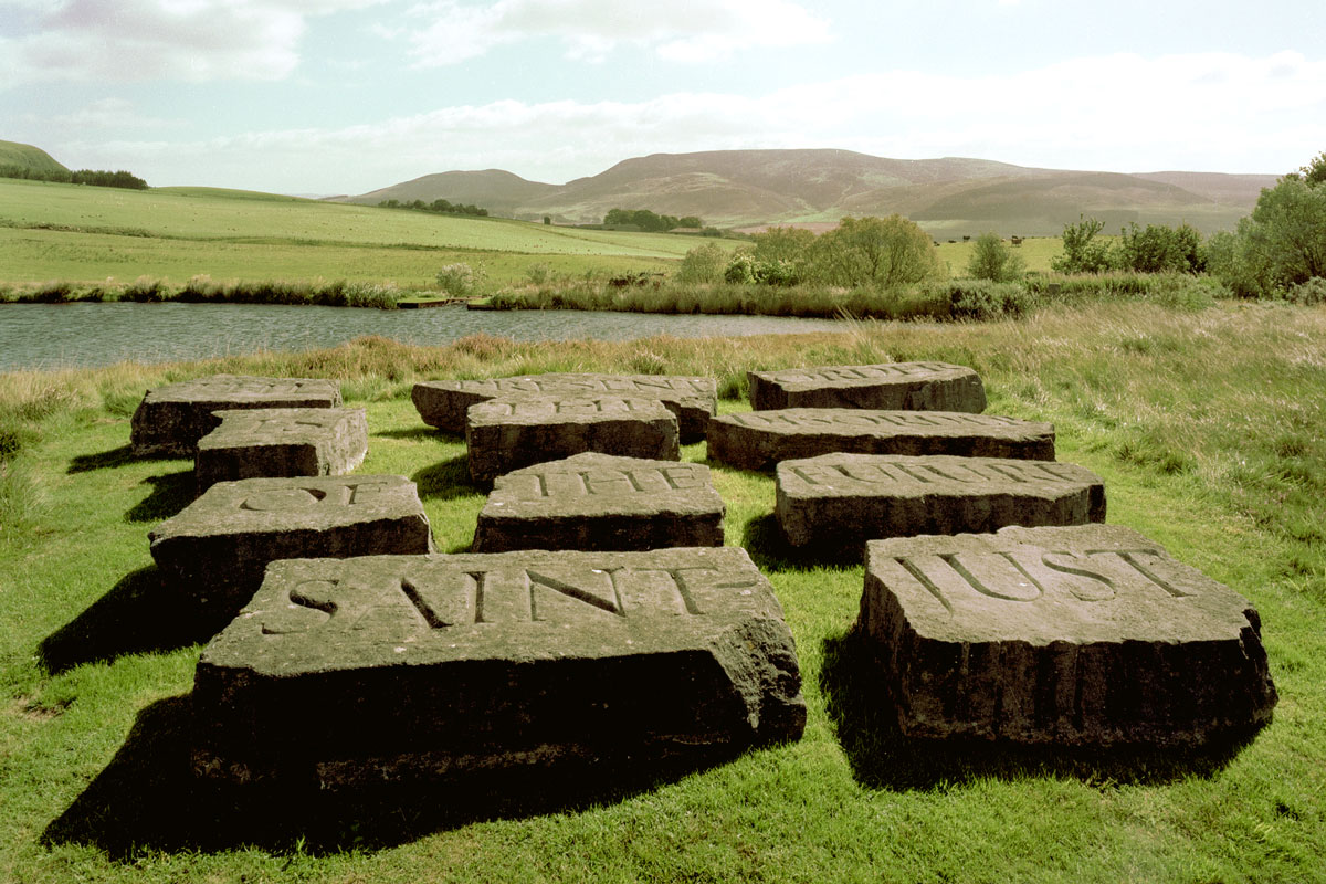 Inscribed slabs of stone arranged in landscape of water, green hills, blue sky
