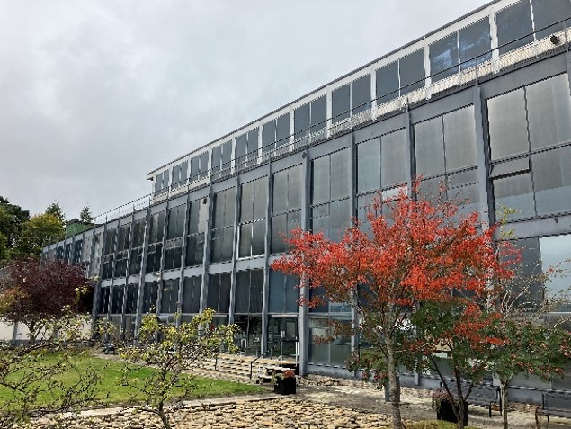 Modern glass, steel and concrete University building with courtyard lawn and planting in foreground.