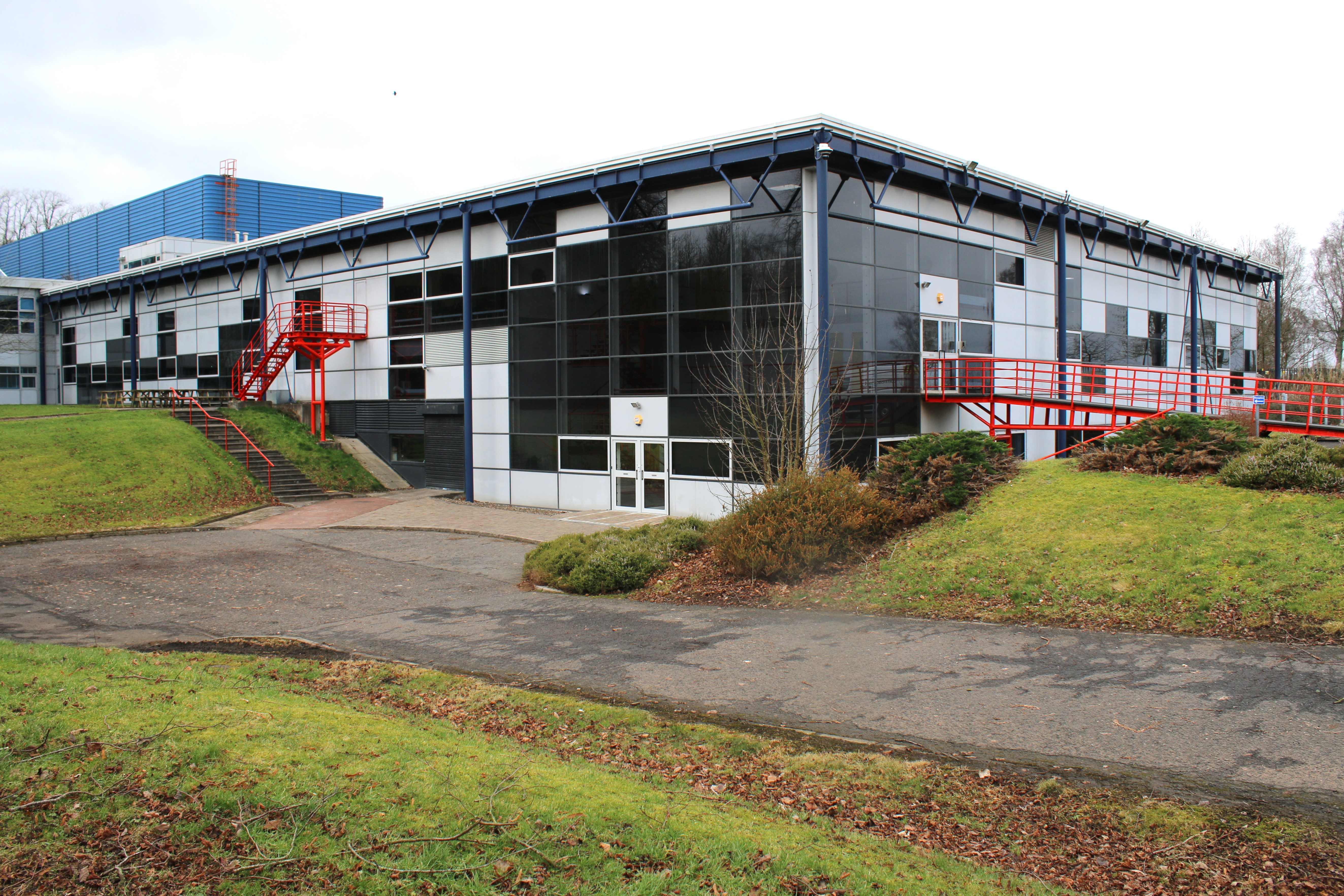 Large factory block, white with black windows, red railings to walkway, white sky background