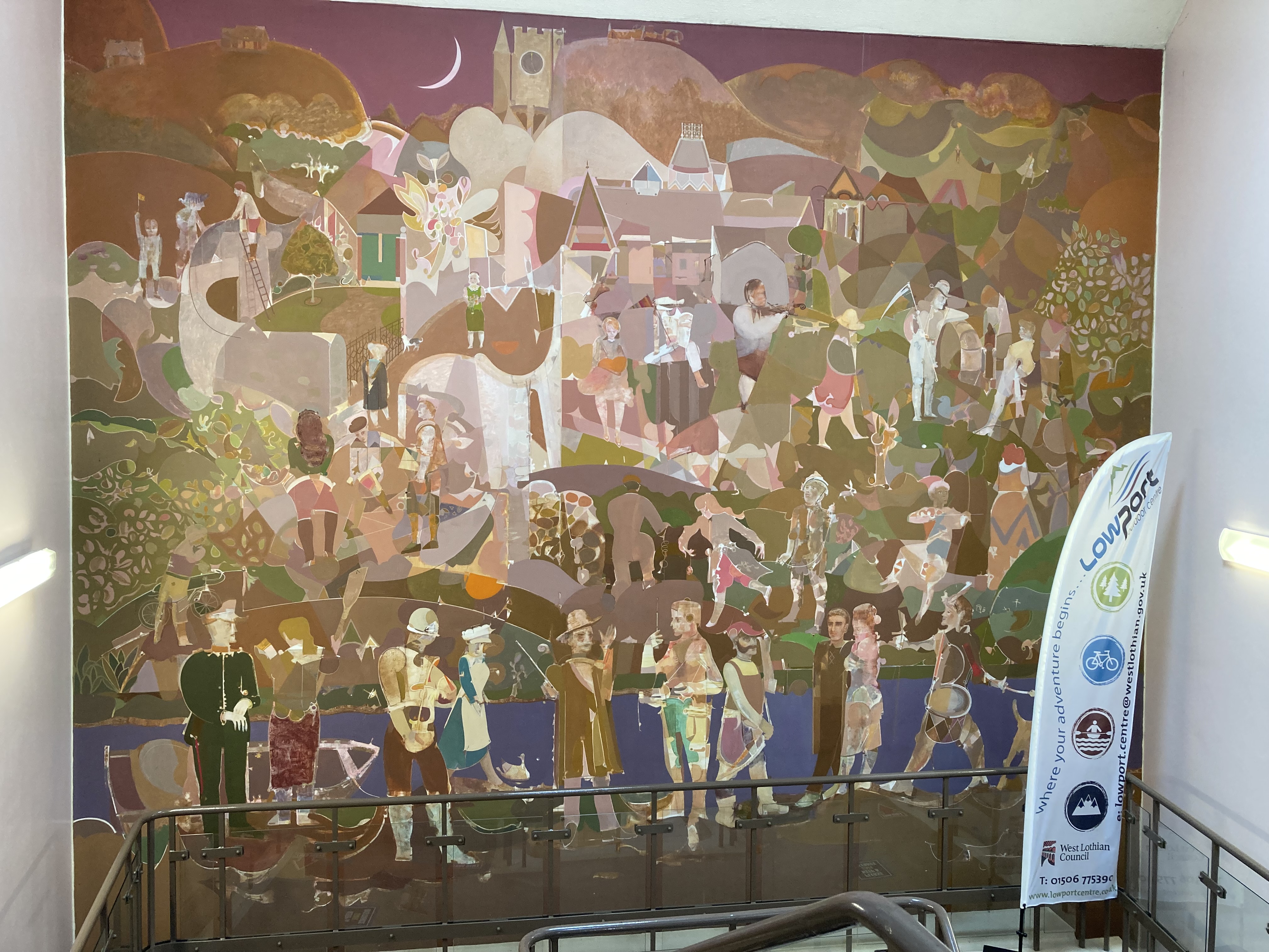 Colourful wall mural inside building showing people, buildings, hills, purple sky