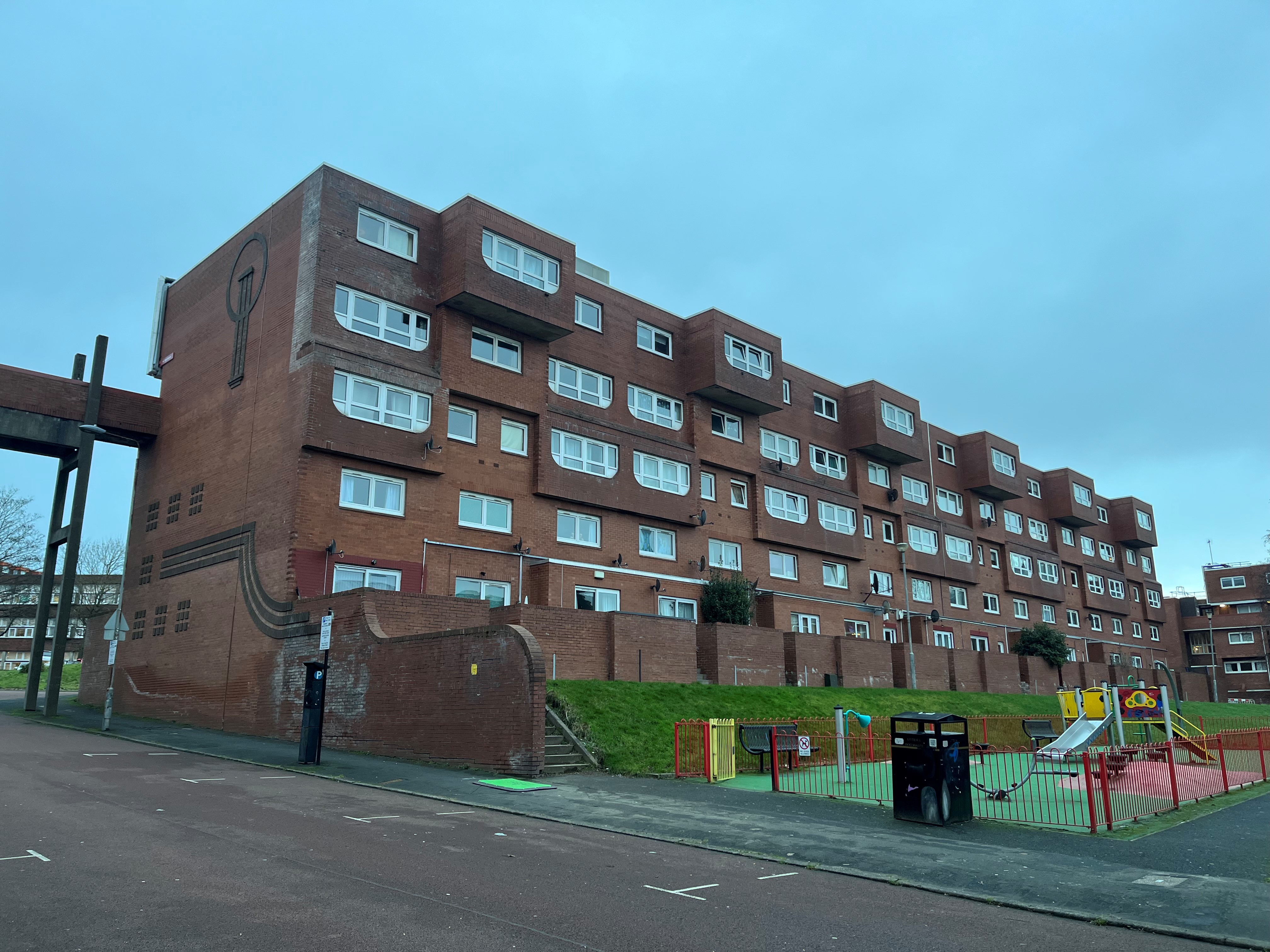 Large red brick housing block, grey-blue sky background, playpark to foreground